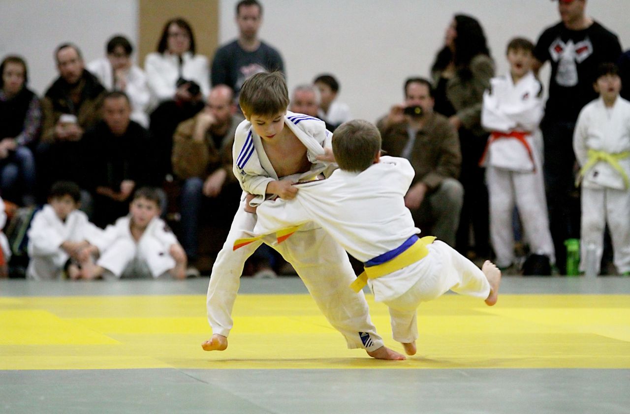 Two young boys compete, one driving into a throw in front of a crowd