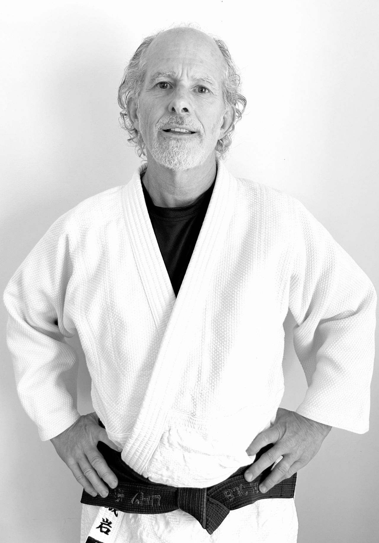 Dave Hocking stands in a white judo gi and black belt, hands on his hips